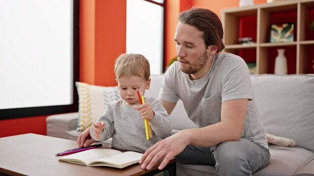 Father and son drawing on notebook sitting on sofa at home