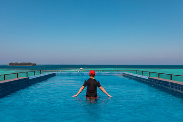Man relaxing in the infinity pool hanging over turquoise lagoon of Karimunjava Indonesian tropical island. 