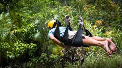 a male tourist flies over a green forest, zip line