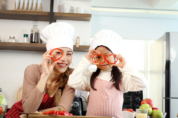 Happy Asian mother and daughter with apron chef hat holding and plying cuted bell pepper during cooking healthy meal at kitchen, lovely family chef cooking food, mom and child spending time together.