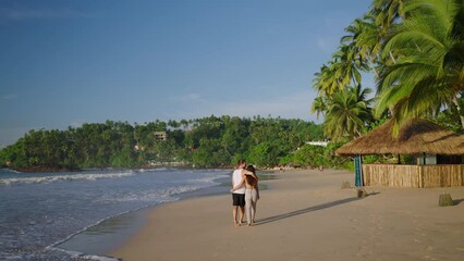 Young biracial happy couple unfocused walking on the beach together enjoying summer backview shot from distance. Smiling boyfriend and girlfriend relaxing and taking a walk at the seaside at sunrise.