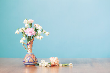 flowers in vintage jug on wooden table on blue background