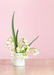 white spring flowers in jug on pink background