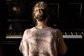 woman playing piano, back view, old rustic black instrument