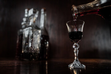 liquor pouring into the crystal glass with crystal bottles at the background, dark colours 