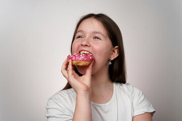 Caucasian Girl in white T-shirt Eating Donut in her hands with pink glaze on white background