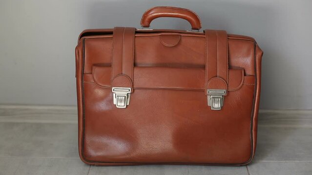 A man lawyer picks up and puts down a brown leather briefcase with documents. 