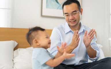 Fototapeta premium Portrait of enjoy happy love family asian father playing with adorable little asian baby.newborn, infant.dad touching with cute son moments good time in a white bedroom.father day, Love of family