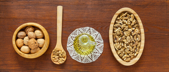 Top view of delicious healthy organic walnut vegetable oil in glass jar, nuts in  wooden bowl and shellless nuts on oval plate on wooden brown table. Close-up, flat lay, copy space, banner, mockup
