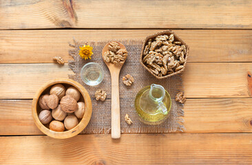 Delicious healthy organic walnut vegetable oil in glass jar, nuts in wooden bowl and shelled nuts on wooden table. Rustic still life. Top view, close-up, flat lay