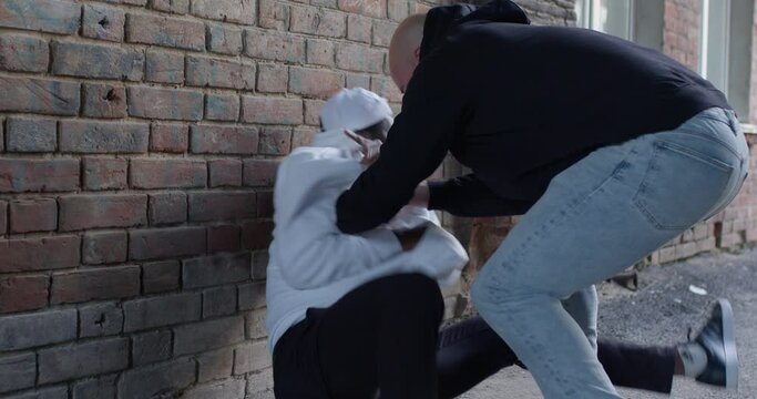Slow motion, Aggressive robber beats frightened male and steal the money at daytime at street. Stranger threatening young black man. Male bandit wear black hoodie. Concept of robbery. City daytime