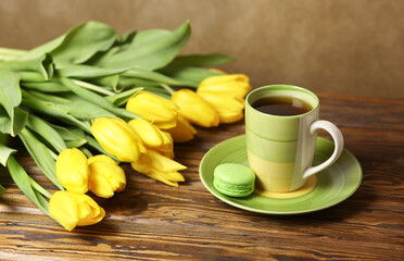 Fototapeta na wymiar A cup of tea with a cake with a bouquet of yellow tulips on a wooden table. Selective focus