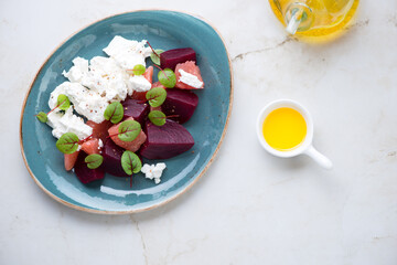 Beetroot, grapefruit and feta cheese salad on a turquoise plate, top view on a light-beige marble background, horizontal shot