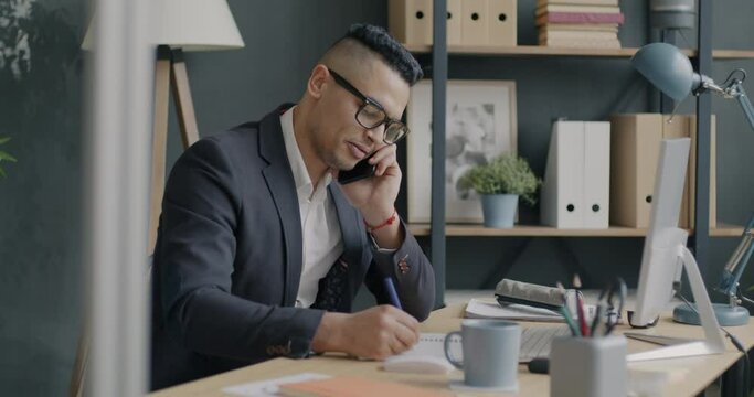 Ambitious employee speaking on mobile phone and writing notes consulting client in office. Modern technology and communication concept.