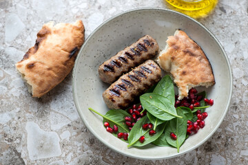Grilled kabobs served with fresh spinach, pomegranate and flatbread in a beige plate, horizontal shot on a brown granite background, elevated view