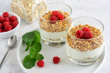 Two glasses of granola with yoghurt, a raspberry on top and mint leaves, close-up