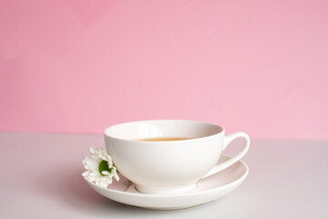 Obraz na płótnie Canvas White set cup and plate with green tea stand on a pink background with chamomile flowers. Minimalism