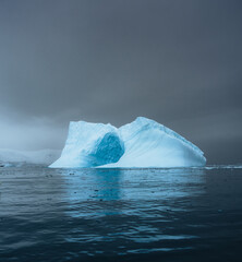 Photogenic and intricate iceberg with a hole under an interesting and colorful sky during. Global warming and climate change concept. Photo taken in Antarctica, Greenland arctic circle.