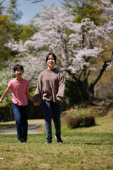 春の桜満開の公園で遊んでいる子供姉妹の様子