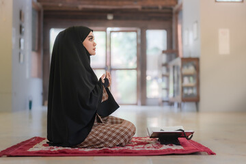 Portrait of a beautiful Asian Muslim woman with her palm open praying to Allah wearing a black...