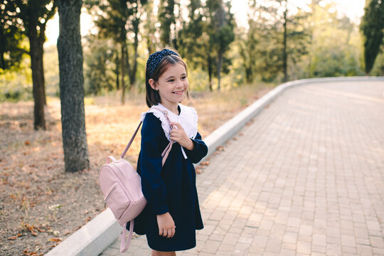 Stylish child girl 6-7 year old wear school dress with collar and background bag walking in city street outdoor. Childhood.