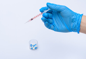 Czerwona mała strzykawka trzymana w dłoni w rękawiczce medycznej nad fiolką z lekarstwami na białym tle - obrazy, fototapety, plakaty