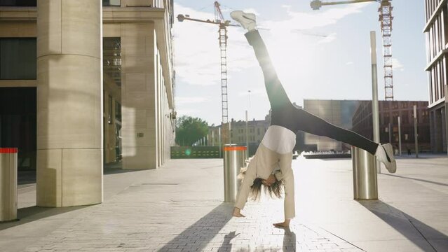 African business woman doing an acrobatic gymnastic wheel on her hands in a business center on a summer day at sunset, a curly-haired office worker with joy does a somersault among the columns in a