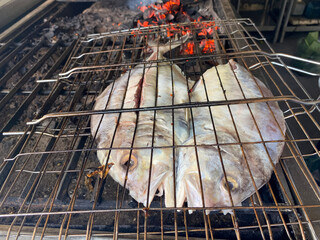 The pompano fish that has been cut in half is grilled over coals using charcoal at restaurant.