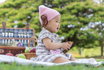 Asian infant (baby girl) sitting on the ground picnic in city park, happy healthy in the holiday vacation summer.