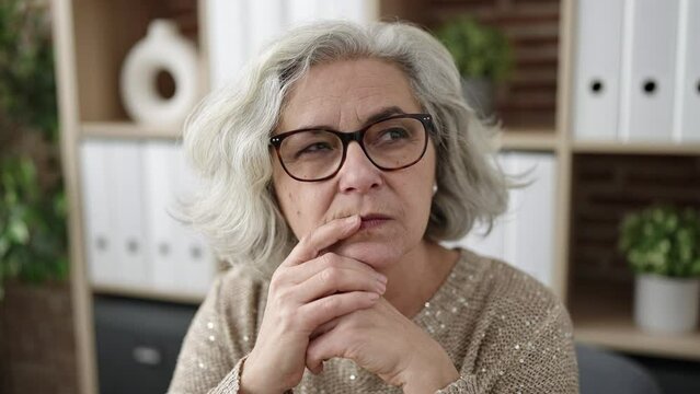 Middle age woman with grey hair business worker sitting with doubt expression at office