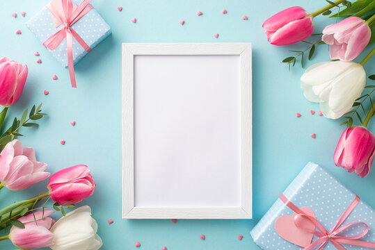 Mother's Day concept. Top view photo of empty photo frame tulips blue gift boxes with ribbon bows and sprinkles on isolated pastel blue background with blank space