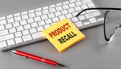 PRODUCT RECALL text on a sticky with keyboard, pen glasses on grey background