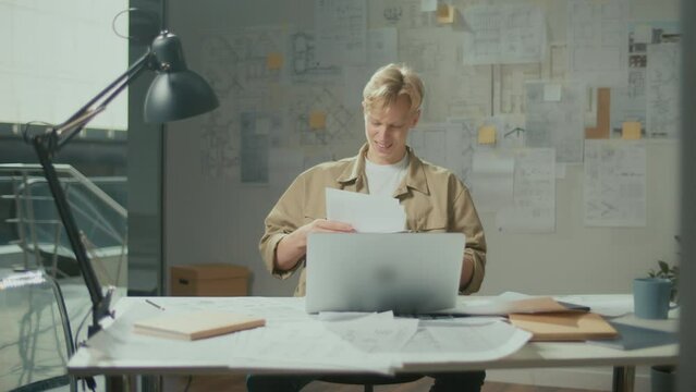 Engineer Bursting with Joy Reviewing Documents. Successful Man Making Profitable Deal and Celebrating the End of the Project.Young Smiling Architect Scatterring Papers around Him Waving Fists Happily