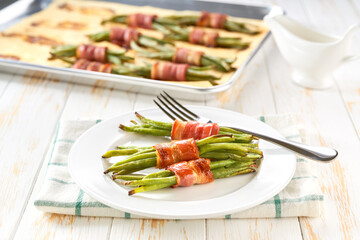 Traditional appetizer, baked  bundles of green beans wrapped in bacon in a ceramic plate on a white...