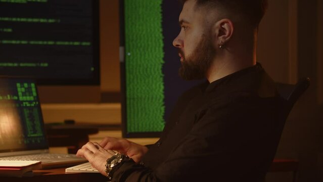 View of a young employee of an IT company working on a laptop in the office. A young programmer sits in front of monitors with running lines of code and is engaged in software testing.