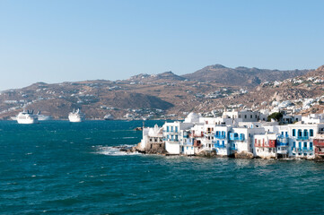 Panoramic view of the village of Chora on the Greek island of Mykonos, in the background the rocky hills and anchored cruise ships. Mediterranean vacation travel concept 