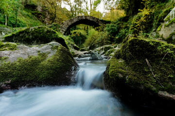 small cascade of water in long exposure in front of an ancient arched stone bridge