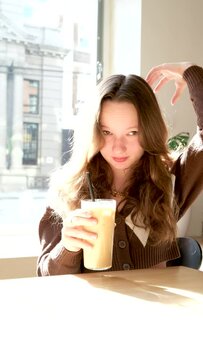 Sad,pensive young woman drinking coffee and looking out of the cafe window. High quality photo
