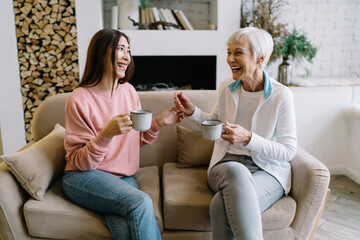 Cheerful senior multiethnic women chatting while having cups of hot drink