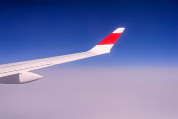 Travel and vacation concept. Wing of an airplane flying above the clouds. Clear blue sky.