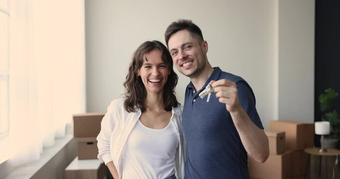 Millennial hispanic couple pose for camera with bunch of keys from their new house, enjoy move-in, relocation day. Transporting company services, bank loan for young family, start new independent life