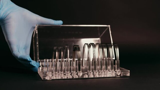 The hand of a dentist close-up opens a case with orthodontic archwires for braces, black background