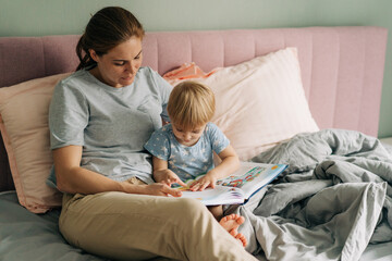 Obraz premium Mom reads a book with her little daughter lying in bed.