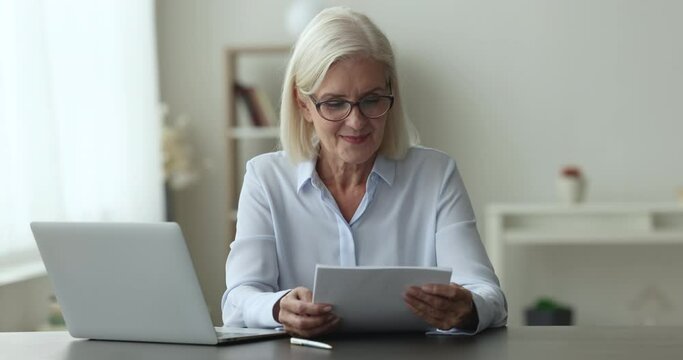 Enthusiastic elderly woman sit at desk with documents, received good news, increase in social pension, bank notice of loan repayment, money back, celebrate achieve, satisfied with insurance agreement