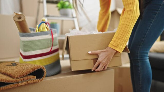 Young beautiful hispanic woman holding cardboard box at new home