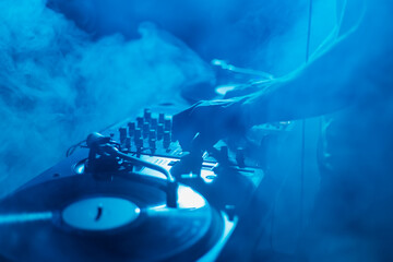 Silhouette of a club DJ mixing music in smoke on stage. Professional disc jokey plays set on techno...