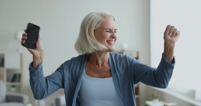 Older woman hold smart phone read received sms, jumps screams with joy celebrate unbelievable news, on-line bet, lottery victory, relish achievement, success, moment of win, candid emotions, happiness