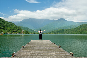 Asian woman standing on an empty pier looking at the view of the lake and mountains at Carp Lake, Taiwan