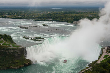 Panoramic view of Niagara Falls tour boat sailing into the Horseshoe Falls waterfall with water mist drifting upwards towards the sky, Ontario, Canada