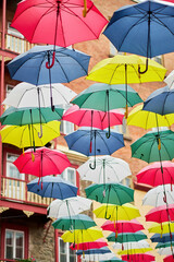 Fototapeta na wymiar Variety of yellow, red, blue, pink and white umbrellas hanging above a street in Quebec, Canada